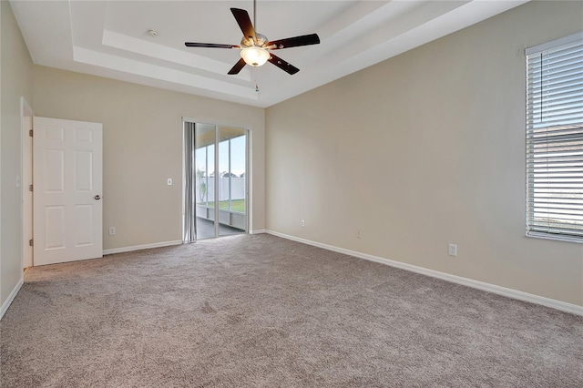 carpeted spare room with a tray ceiling and ceiling fan