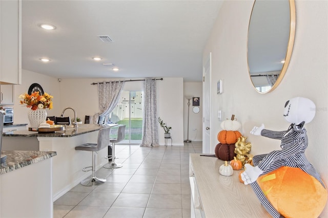 kitchen featuring white cabinetry, sink, a kitchen breakfast bar, dark stone countertops, and light tile patterned floors