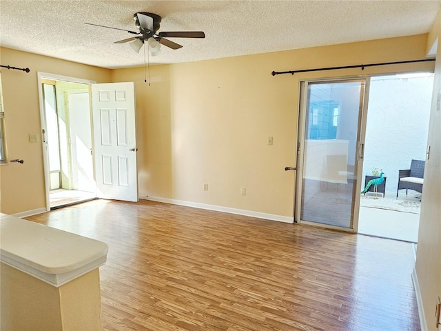 unfurnished living room with a textured ceiling, ceiling fan, light wood finished floors, and baseboards