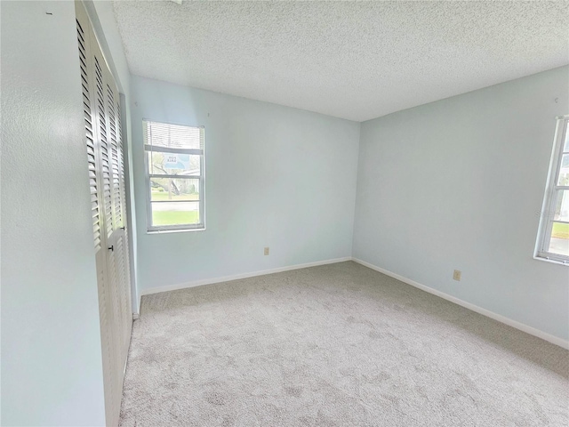 spare room featuring light colored carpet, a textured ceiling, and baseboards