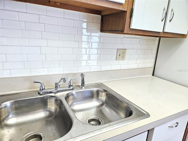 interior details featuring white cabinets, decorative backsplash, light countertops, and a sink