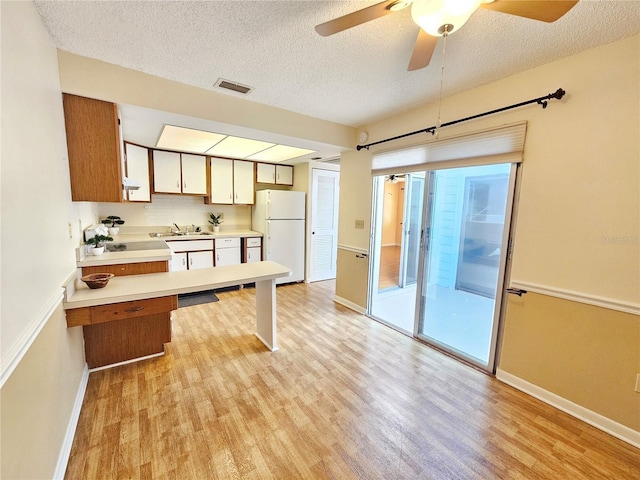 kitchen with light countertops, visible vents, freestanding refrigerator, a sink, and light wood-type flooring