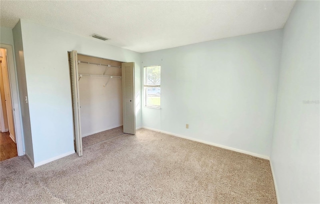 unfurnished bedroom with a textured ceiling, visible vents, baseboards, a closet, and carpet