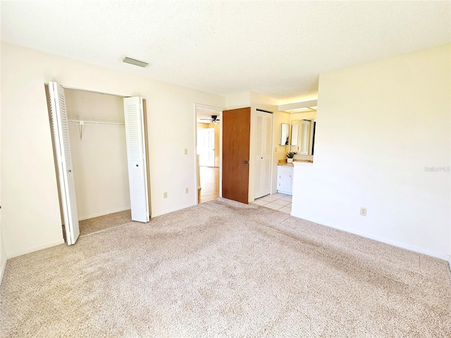 unfurnished bedroom with multiple closets, visible vents, light carpet, and a textured ceiling