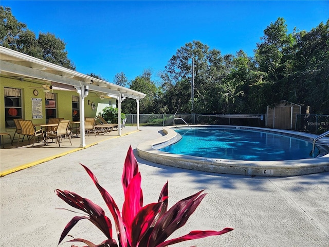 community pool with a patio area, a storage shed, fence, and an outbuilding