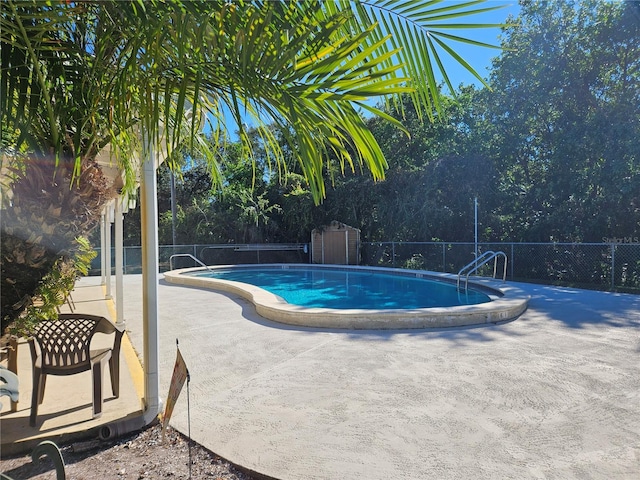 community pool featuring a storage shed, a patio area, fence, and an outbuilding