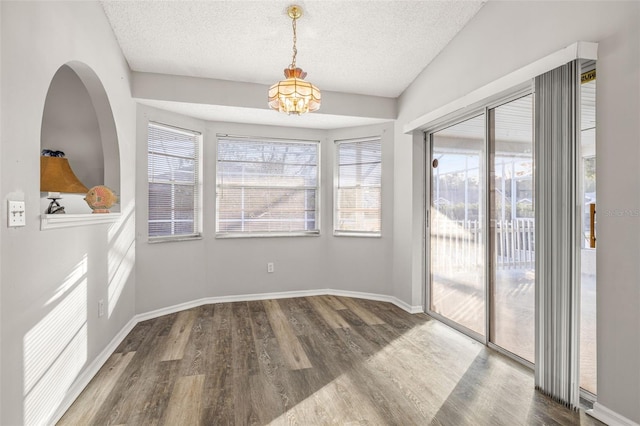 unfurnished dining area featuring hardwood / wood-style floors, a wealth of natural light, a textured ceiling, and an inviting chandelier