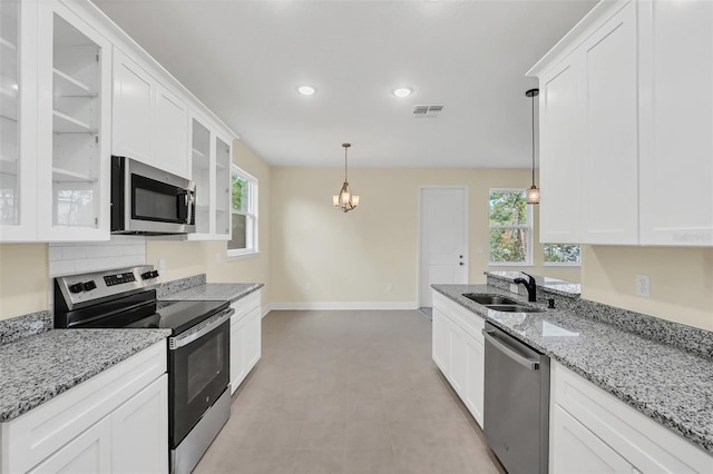 kitchen featuring light stone counters, white cabinets, hanging light fixtures, sink, and appliances with stainless steel finishes