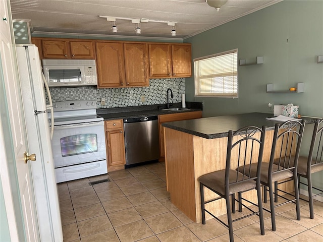 kitchen featuring a kitchen bar, sink, white appliances, and light tile patterned flooring