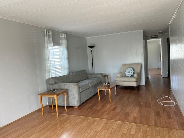 living room with ornamental molding, hardwood / wood-style floors, and wooden walls