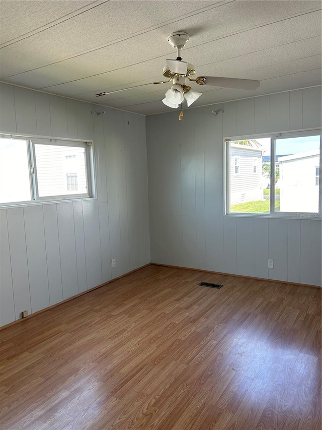 unfurnished room with wood walls, ceiling fan, a healthy amount of sunlight, and light hardwood / wood-style flooring