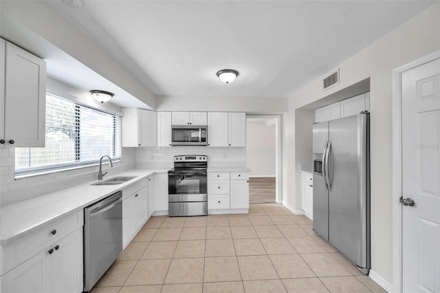 kitchen featuring decorative backsplash, stainless steel appliances, sink, light tile patterned floors, and white cabinets