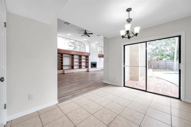 empty room with ceiling fan with notable chandelier and light hardwood / wood-style flooring