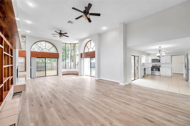 unfurnished living room with ceiling fan with notable chandelier, a high ceiling, and light wood-type flooring