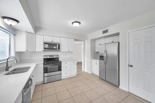 kitchen with sink, light tile patterned floors, tasteful backsplash, white cabinets, and appliances with stainless steel finishes