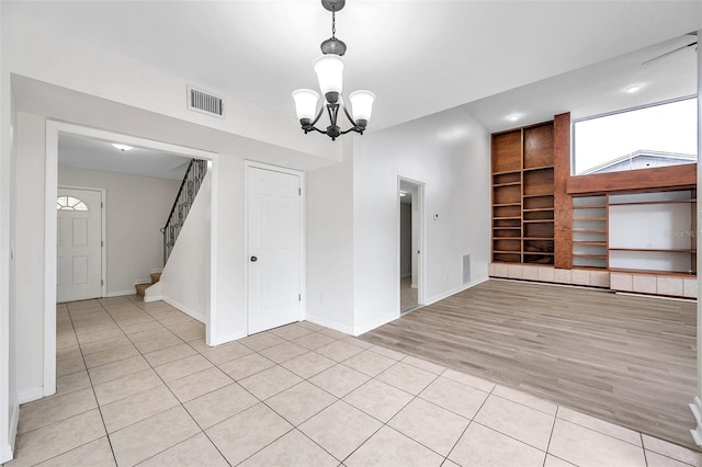 empty room with built in features, light tile patterned floors, and a chandelier