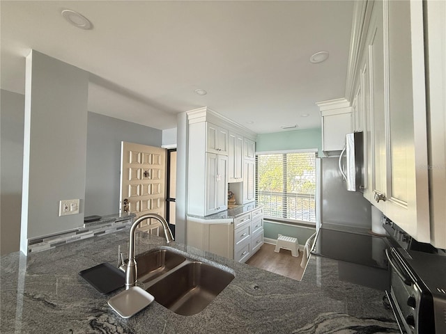 kitchen featuring dark stone countertops, white cabinetry, kitchen peninsula, and sink