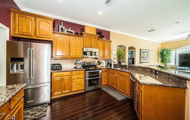 kitchen with appliances with stainless steel finishes, dark hardwood / wood-style flooring, dark stone counters, crown molding, and sink