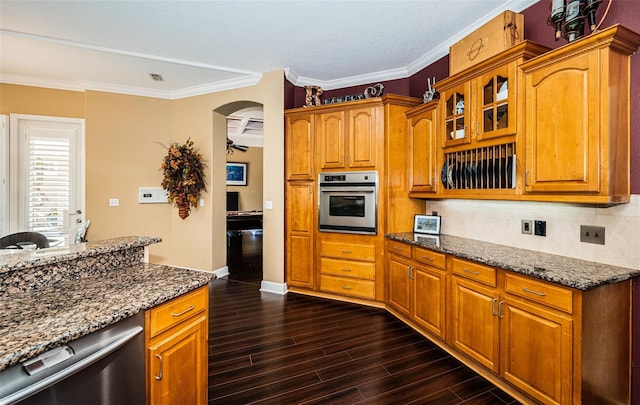 kitchen with crown molding, ceiling fan, dark stone countertops, dark hardwood / wood-style flooring, and stainless steel appliances