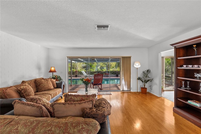 living room with a textured ceiling, light wood-type flooring, brick wall, and a healthy amount of sunlight