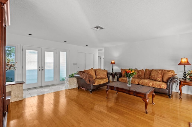 living room with a textured ceiling, light wood-type flooring, and french doors