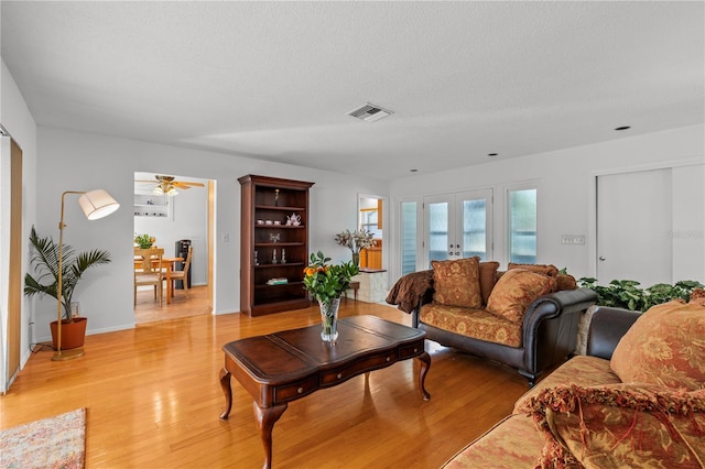 living room featuring light wood-type flooring, a textured ceiling, ceiling fan, and french doors