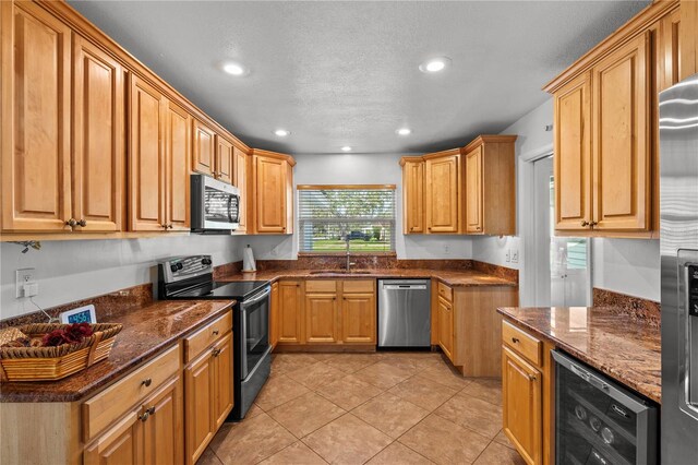 kitchen with dark stone counters, beverage cooler, sink, and appliances with stainless steel finishes