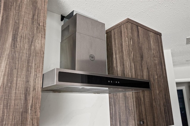 details featuring wall chimney range hood and a textured ceiling