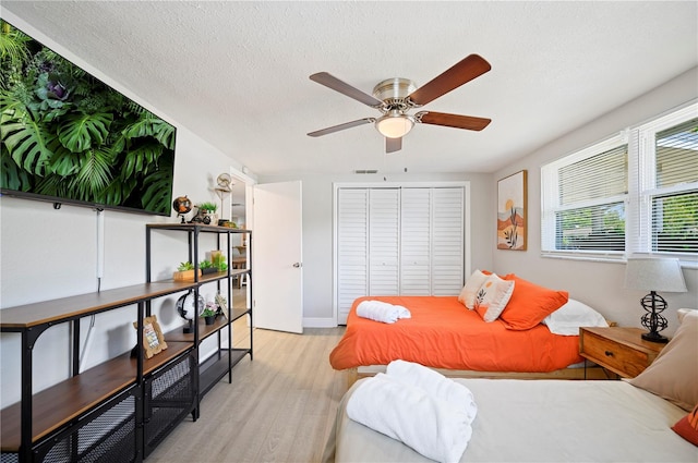 bedroom with a closet, light wood-type flooring, a textured ceiling, and ceiling fan