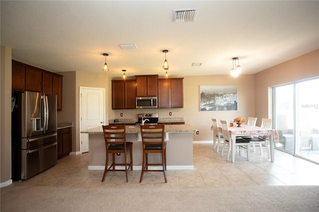 kitchen with light stone countertops, appliances with stainless steel finishes, a breakfast bar, a kitchen island with sink, and decorative light fixtures