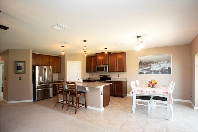 kitchen featuring light stone counters, decorative light fixtures, a kitchen bar, a kitchen island with sink, and appliances with stainless steel finishes