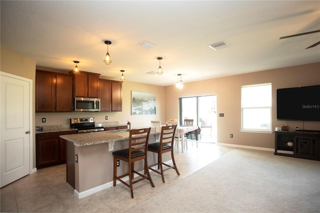 kitchen with appliances with stainless steel finishes, a kitchen breakfast bar, a kitchen island with sink, sink, and pendant lighting