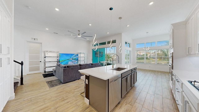 kitchen with stainless steel dishwasher, a kitchen island with sink, sink, pendant lighting, and white cabinetry