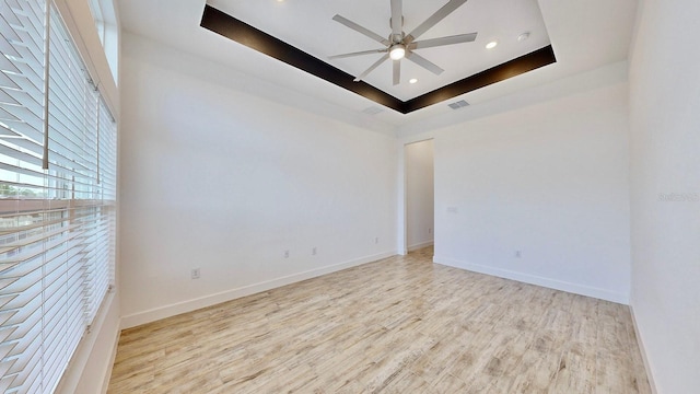 empty room with a raised ceiling, ceiling fan, and light hardwood / wood-style flooring