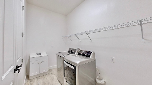 laundry area with light hardwood / wood-style floors, cabinets, separate washer and dryer, and sink