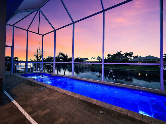 pool at dusk featuring a patio area, pool water feature, a water view, and glass enclosure