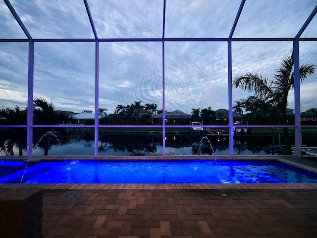 pool at dusk with pool water feature, a lanai, a patio area, and a water view