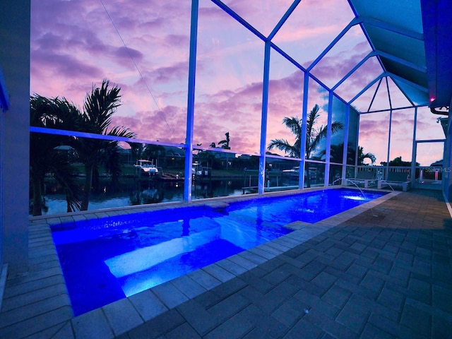 pool at dusk with a water view, a patio area, and a lanai