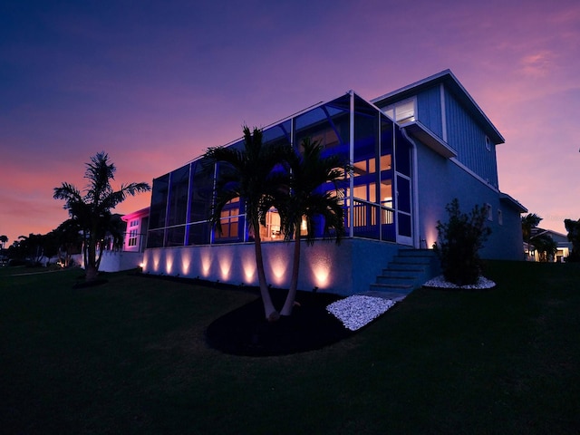 back house at dusk featuring a lanai and a yard