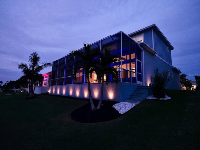 back house at dusk featuring a lawn and a lanai