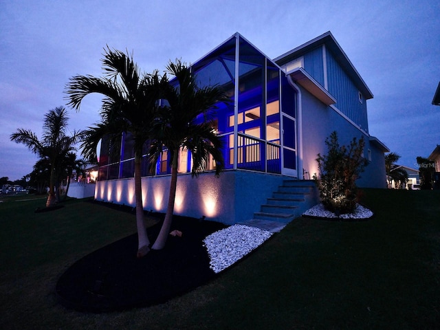 back house at dusk with a lawn and a sunroom