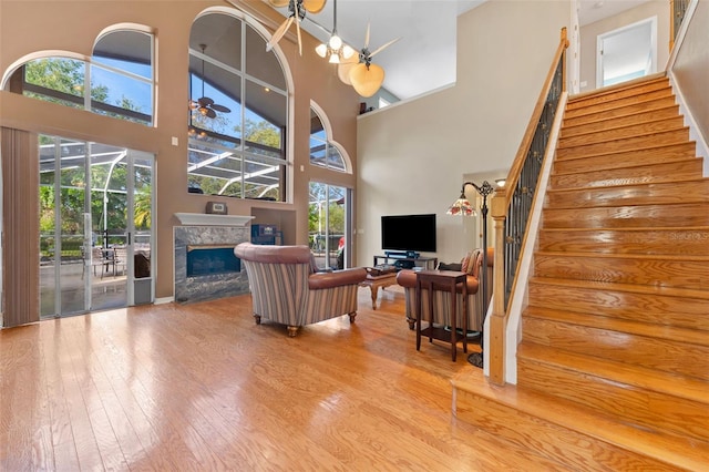 living room with hardwood / wood-style flooring, a high ceiling, a premium fireplace, and ceiling fan with notable chandelier