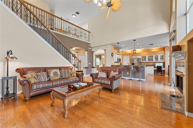 living room with light wood-type flooring, ceiling fan, and a towering ceiling