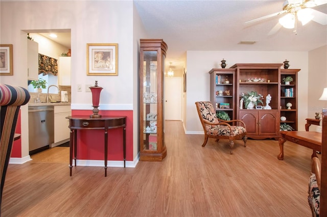 living area featuring a textured ceiling, light wood-type flooring, ceiling fan, and sink