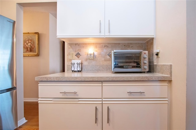 interior details featuring stainless steel fridge, white cabinetry, light hardwood / wood-style flooring, and decorative backsplash