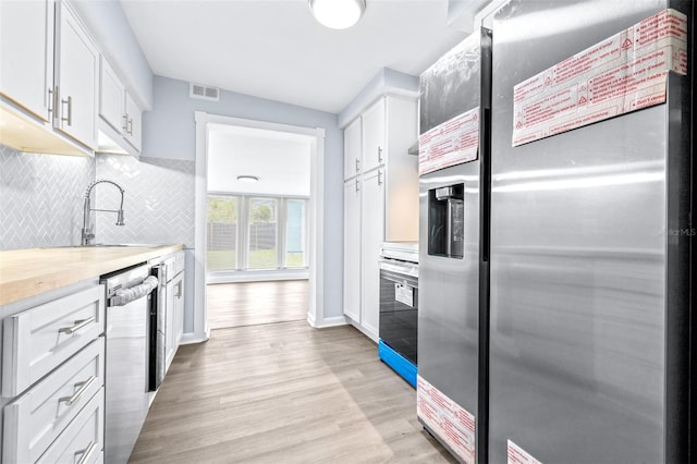 kitchen featuring tasteful backsplash, white cabinetry, appliances with stainless steel finishes, light wood-type flooring, and sink