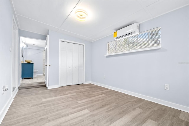 unfurnished bedroom featuring a closet, a wall mounted air conditioner, light hardwood / wood-style floors, and ensuite bathroom