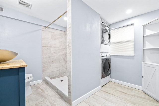 bathroom with a shower, vanity, toilet, and stacked washer / drying machine