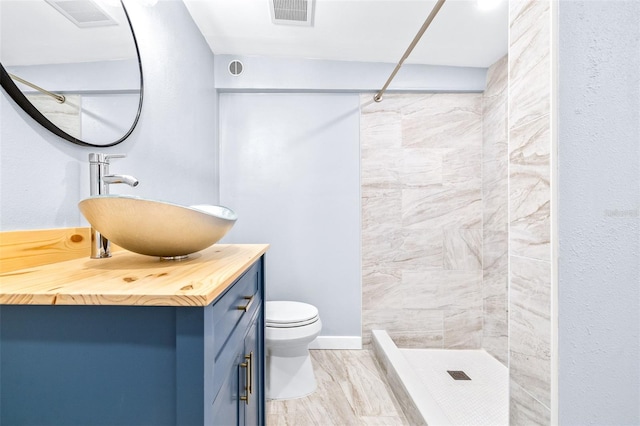 bathroom featuring toilet, vanity, and a tile shower