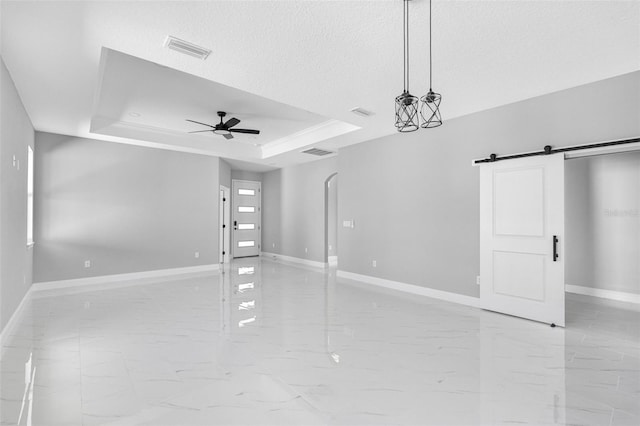 spare room with a textured ceiling, a barn door, ceiling fan, and a tray ceiling